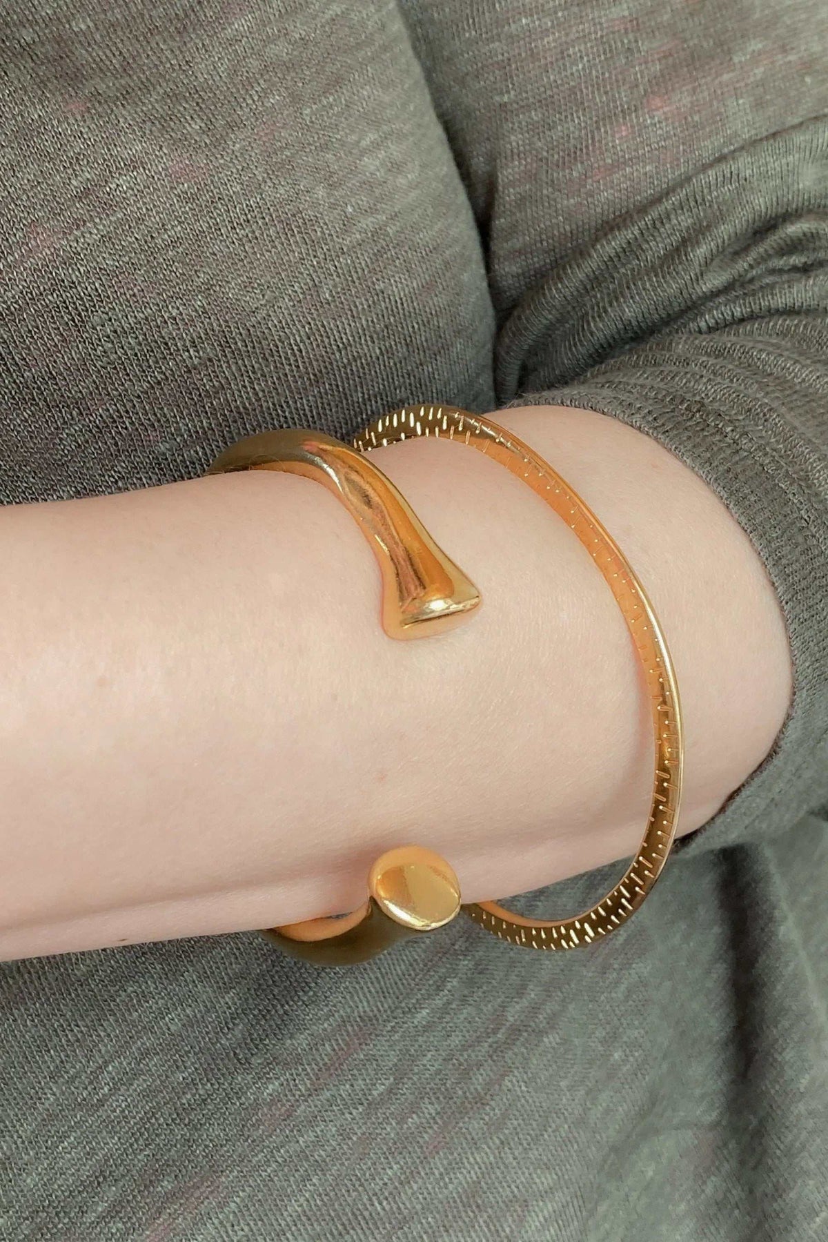 URGO Gold Bracelet in polished gold-tone metal, an open cuff with tapered sculptural ends and a textured rim