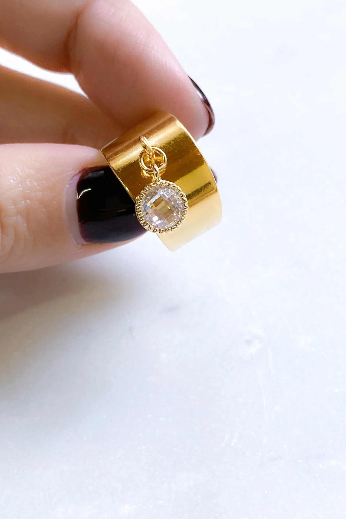 Wide flat band ring in polished gold-tone metal with a clear faceted charm surrounded by tiny stones