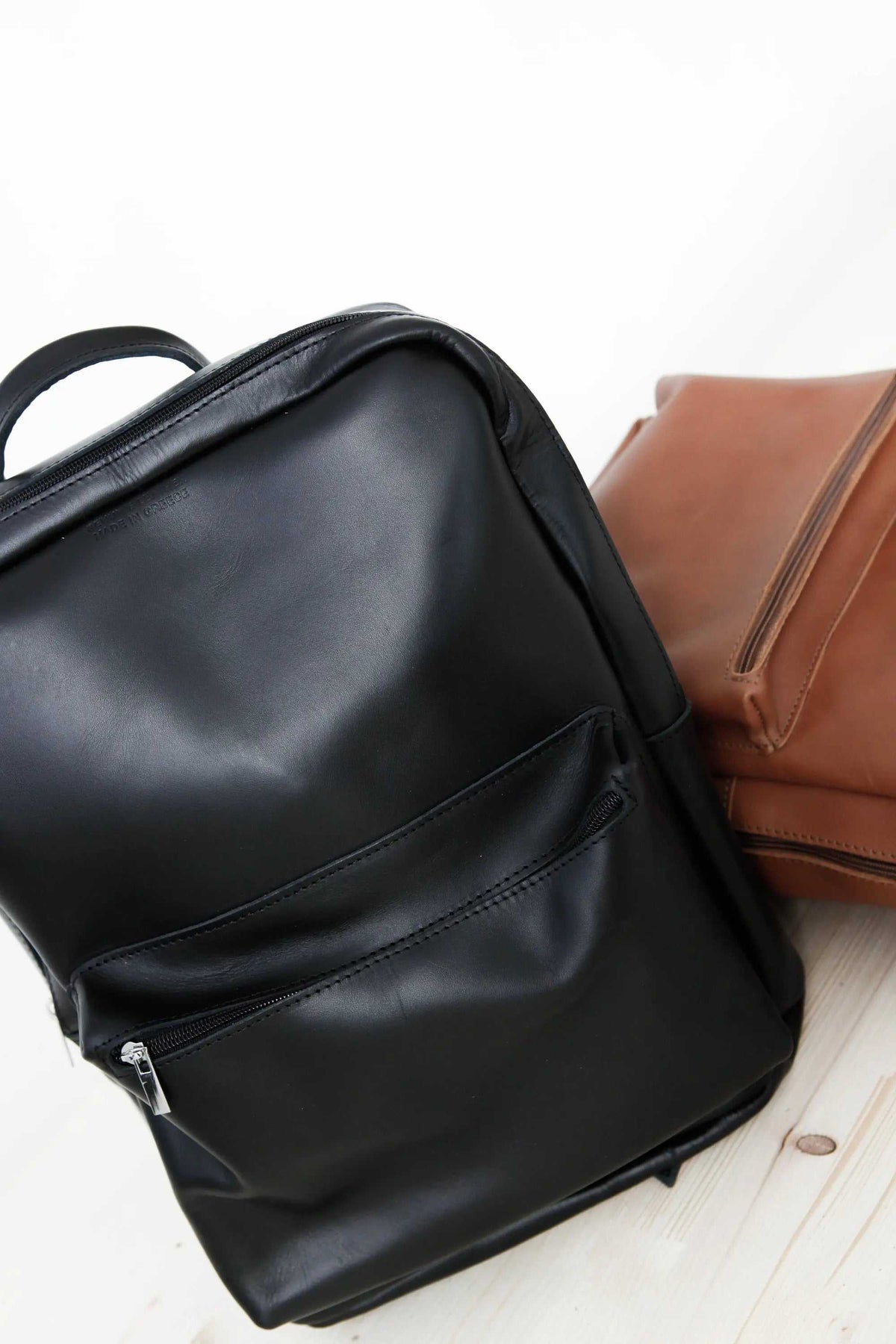 XLARGE BACKPACK leather rucksack in black with front zip pocket, beside a camel backpack
