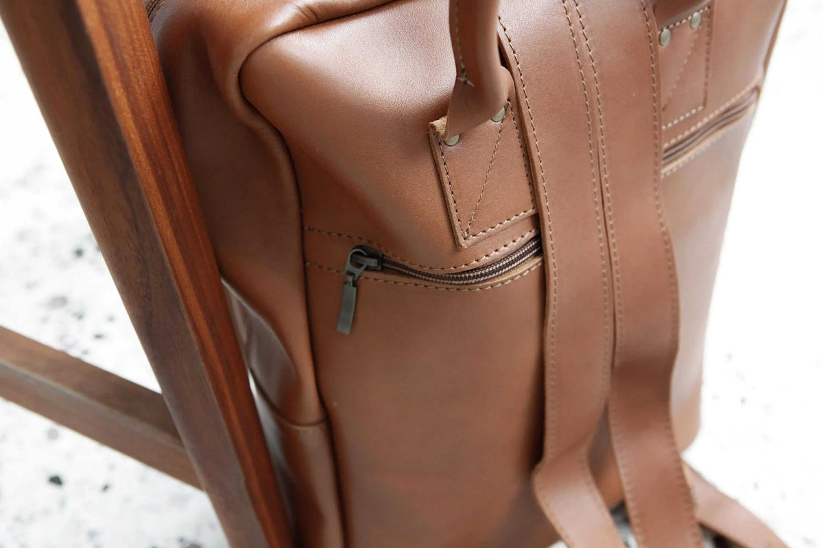 XLARGE BACKPACK in smooth camel-brown leather, featuring a zippered side pocket, stitched straps and metal rivets